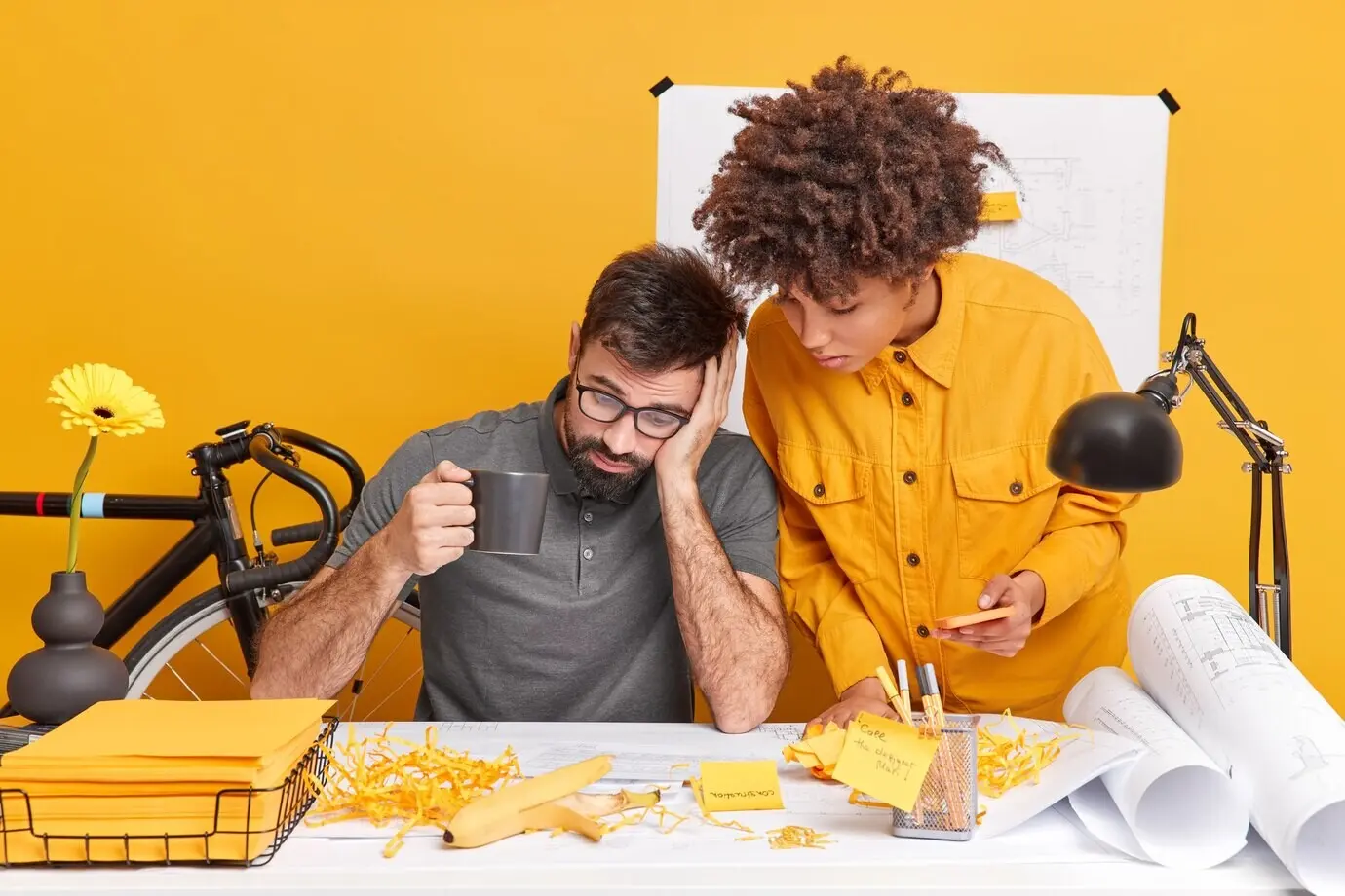 Two women and one man, business partners, share information and work together on a new project, focusing attentively on papers and new building blueprints, posed in a coworking space. Collaboration concept.